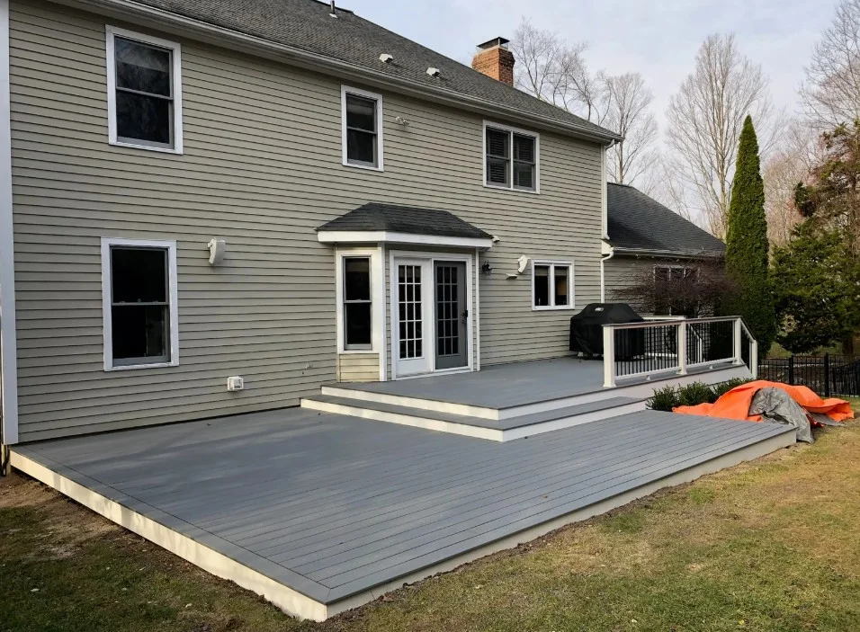 Two-level gray deck with white trim and black railings off the back of a two-story home